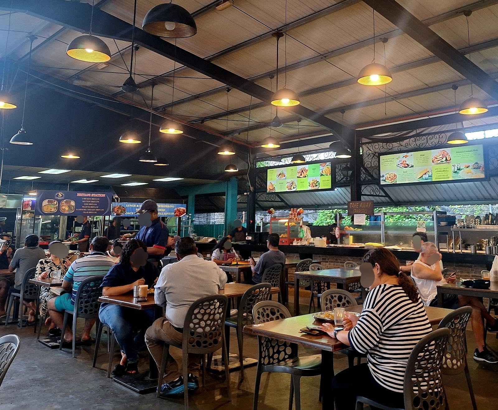 The open-air dining hall under a steel-truss roof with hanging lamps, ceiling fans and a busy lunchtime crowd